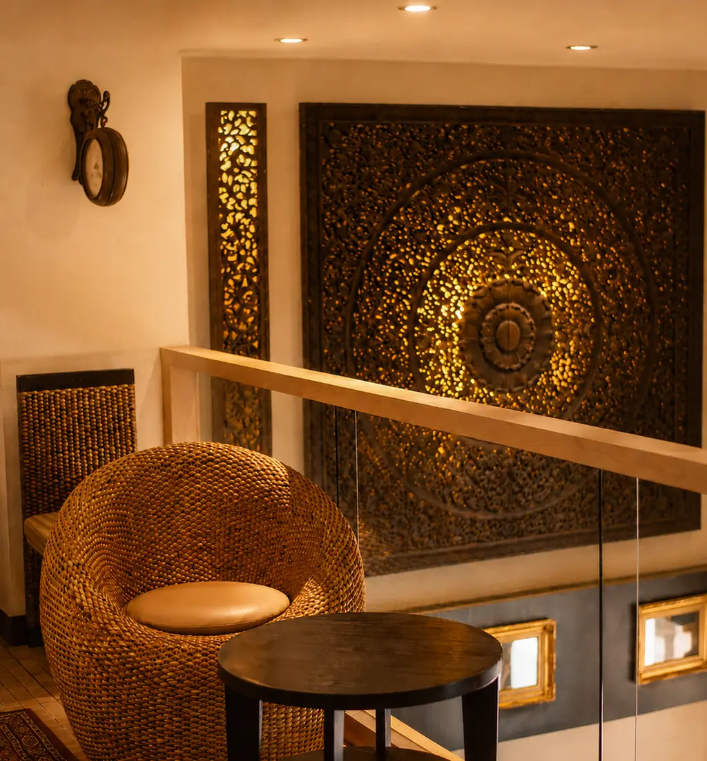 The upstairs lounge at Ananda — a rattan chair beside a carved teak panel